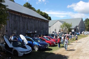 Photo Credit: David Harris. Plug-in vehicles lined up in front of the two big barns at the New London Historical Society during our Electric Vehicle Expo. From left: white BMW i8, blue Tesla Model X, two red Chevy Volts, black BYD e6, three Tesla Model S's, a BMW i3, blue Nissan Leaf, white Nissan Leaf. 